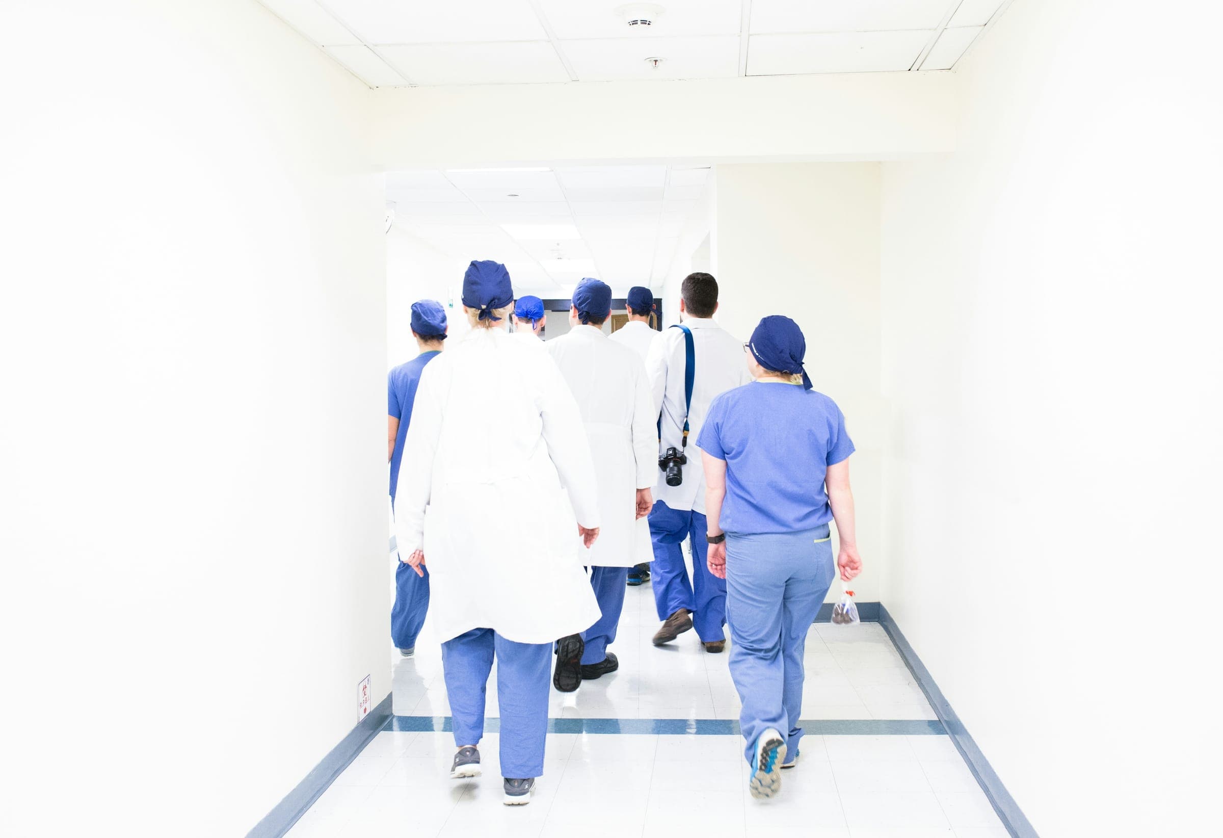 Une équipe soignante en blouses et tenues de bloc marchant ensemble dans un couloir d’hôpital